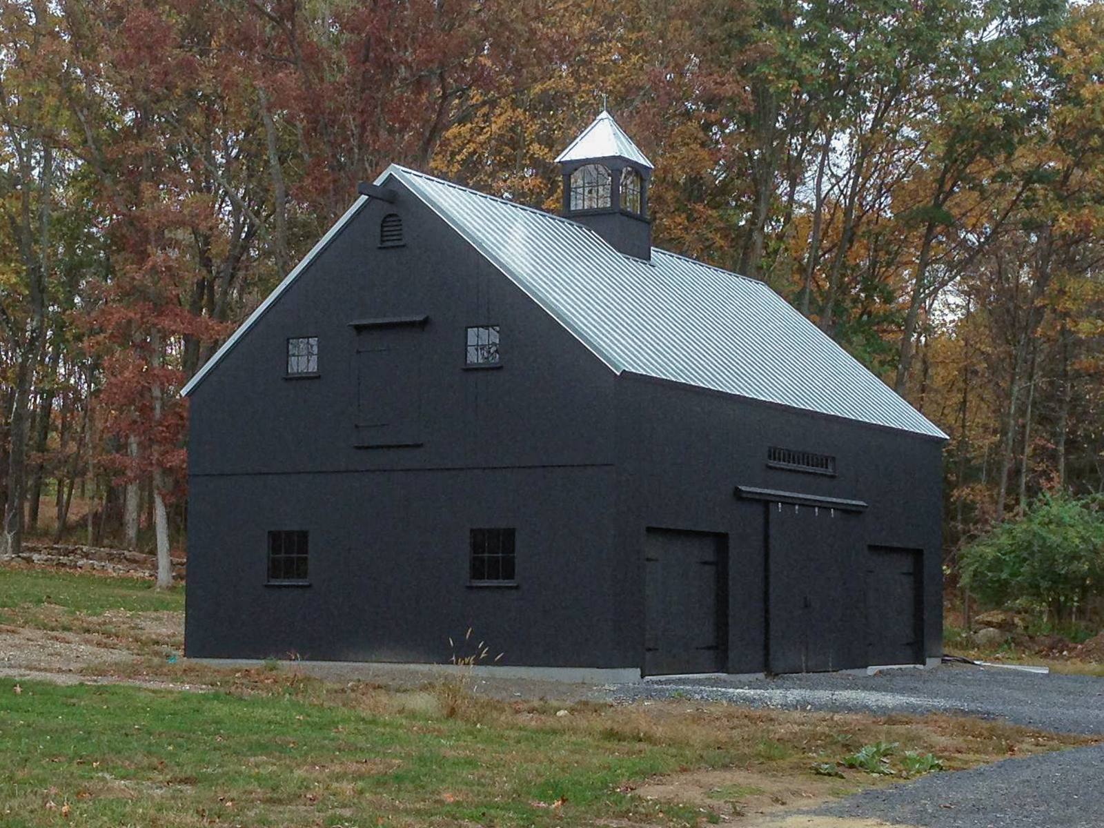Black barn with a metal roof and cupola in autumn woods