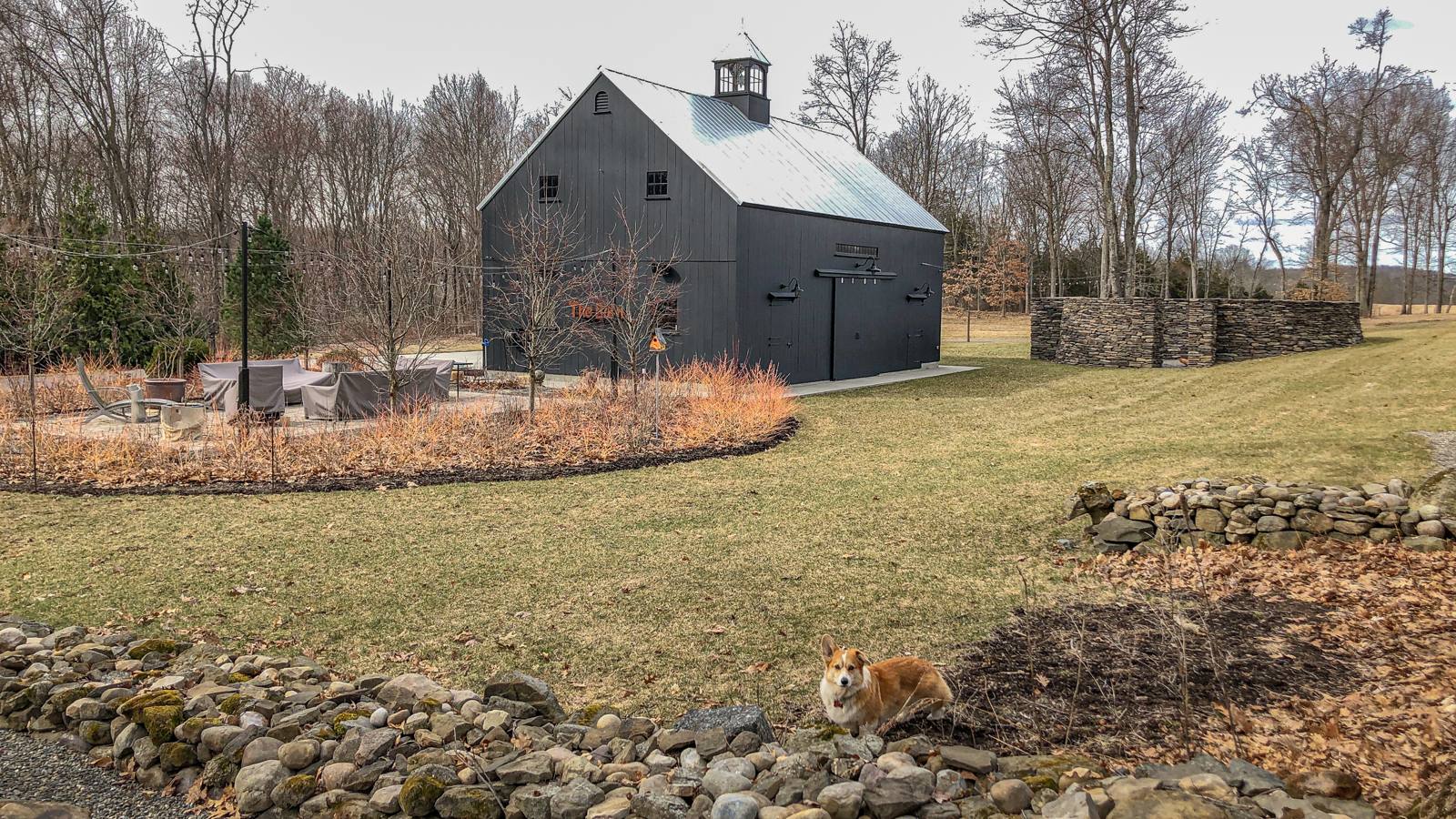 Barn, firepit terrace and a stone ruin wall seen across the lawn