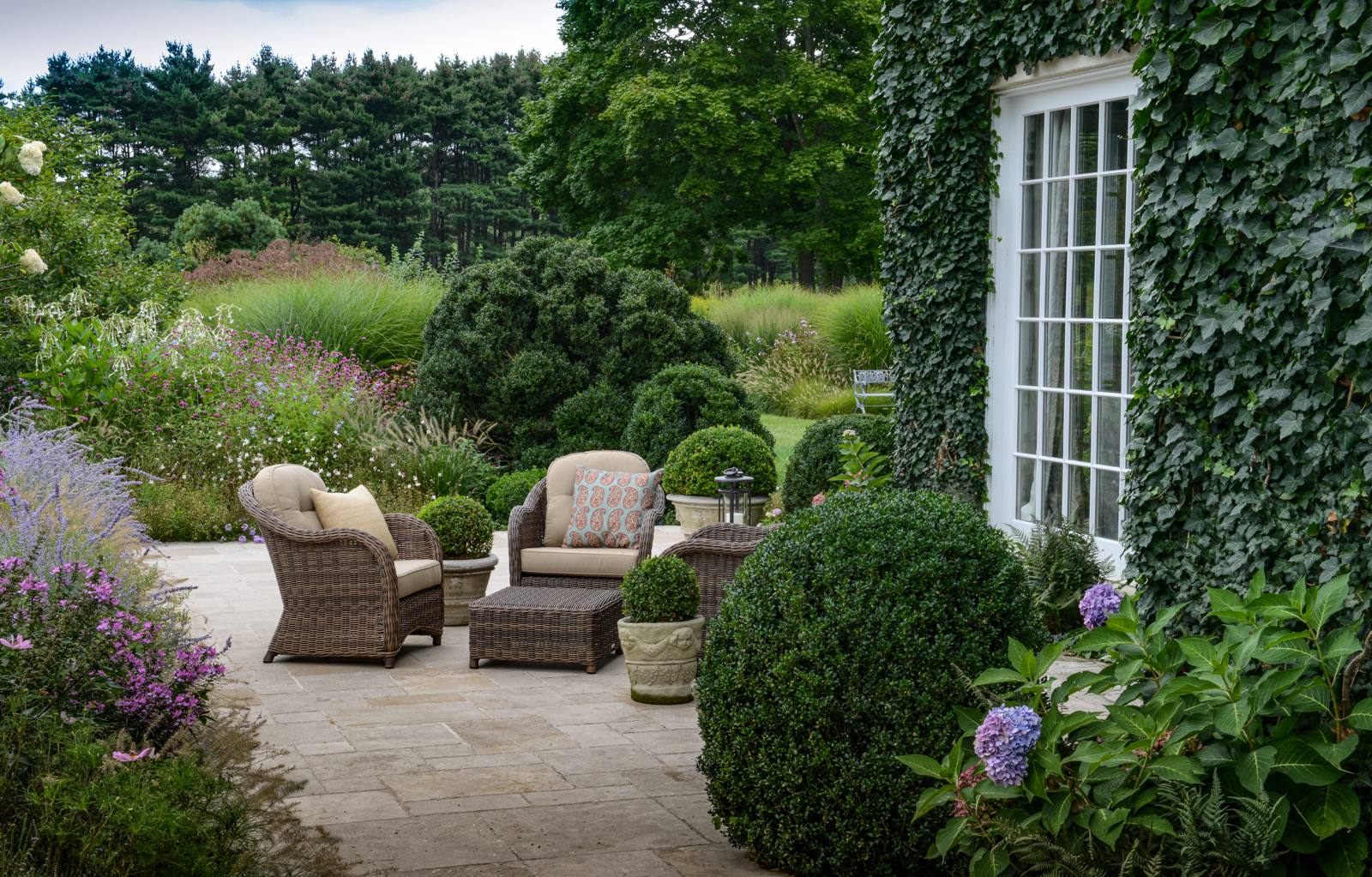 Seating area on a limestone terrace among boxwood and perennials