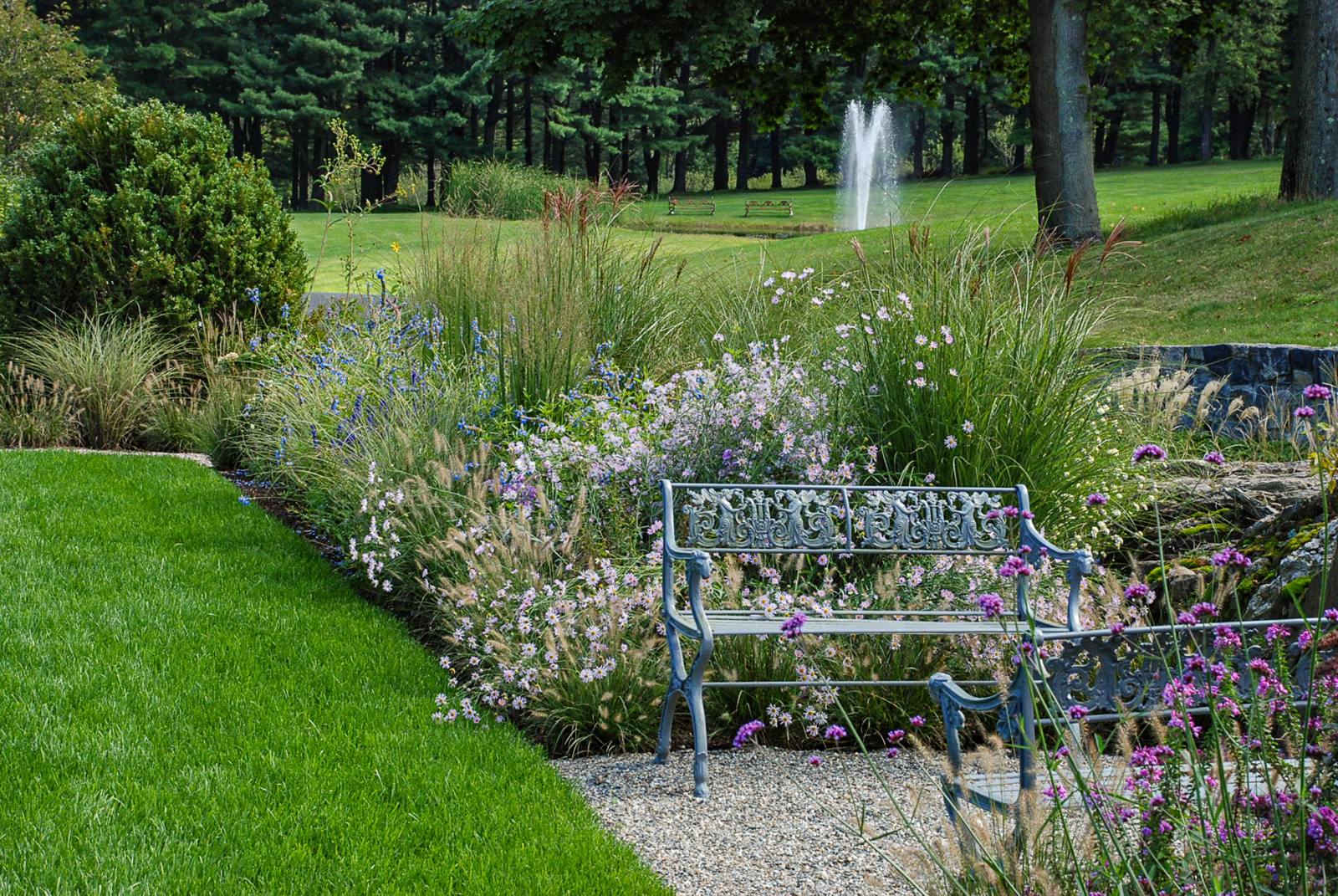 Iron bench in a perennial border with a fountain beyond the lawn