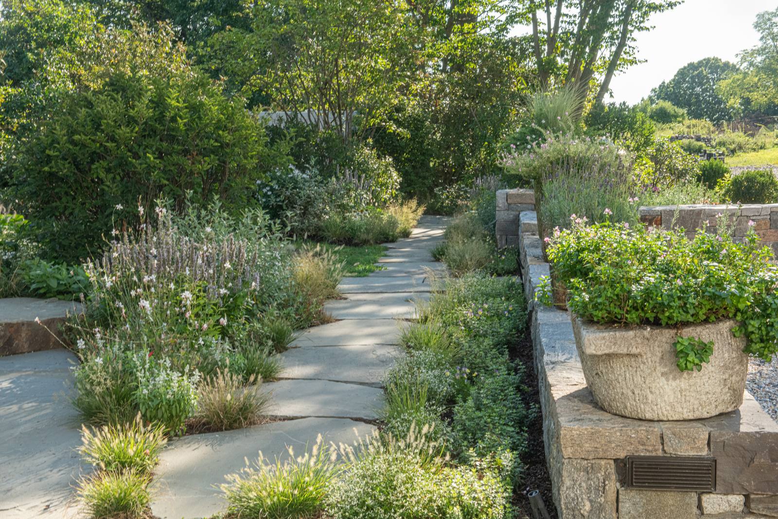 Bluestone path beside a stone wall with a stone trough planter