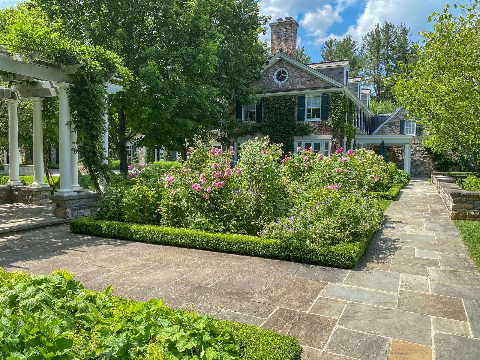 Rose garden edged in boxwood beside a stone and brick house