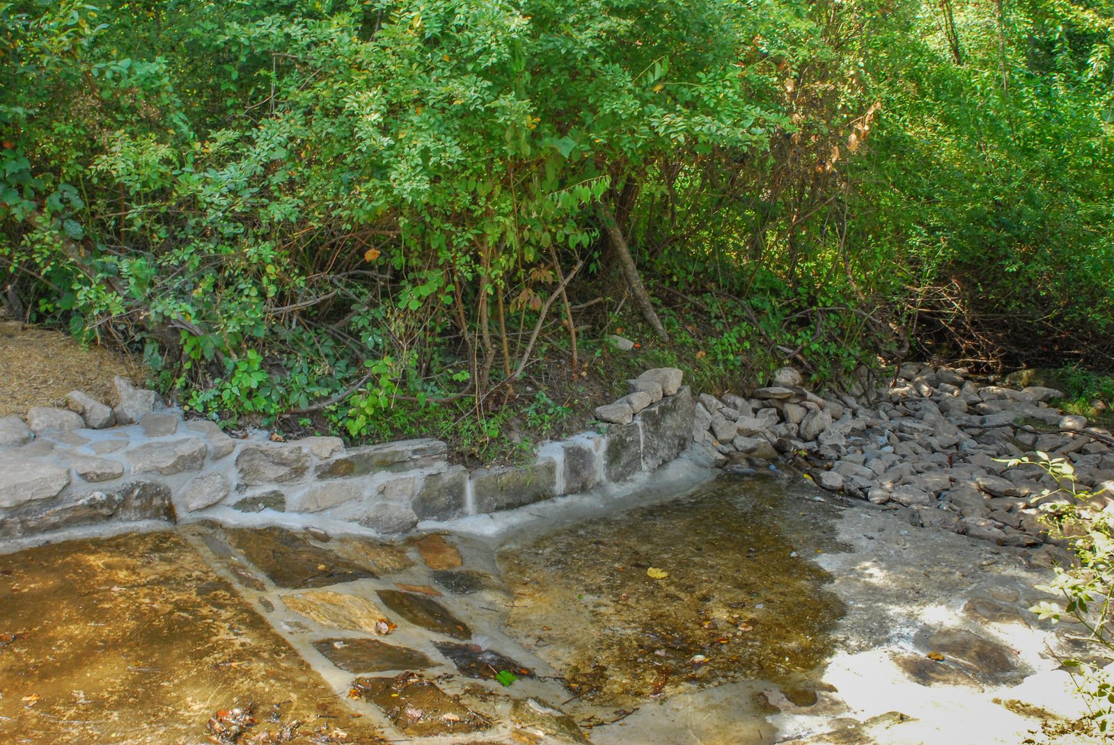 Mortared stone wall and stone-lined spring pool beside a rock spillway